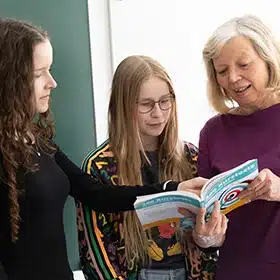 Lehrerin und zwei Schülerinnen betrachten ein Buch