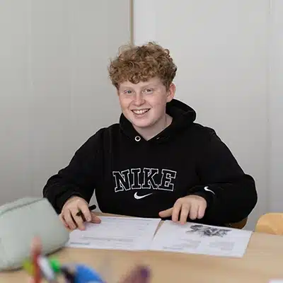 Jugendlicher mit Locken sitzt am Tisch mit Unterlagen