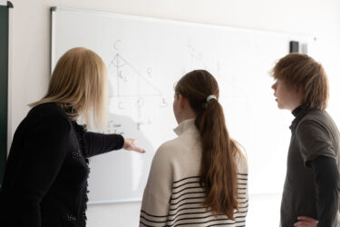Nachhilfelehrerin erklärt zwei Jugendlichen eine Geometrieaufgabe am Whiteboard