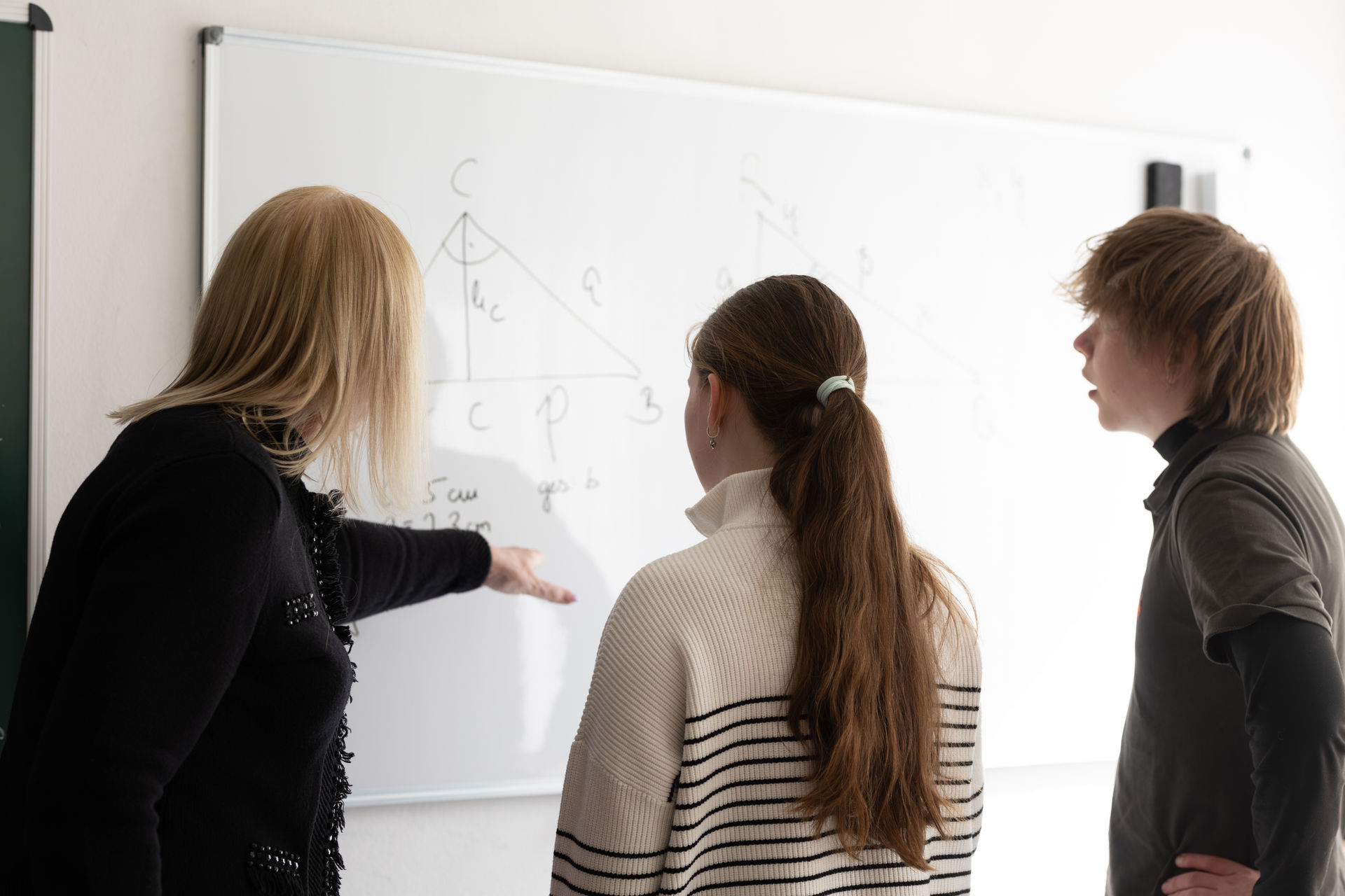 Nachhilfelehrerin erklärt zwei Jugendlichen eine Geometrieaufgabe am Whiteboard