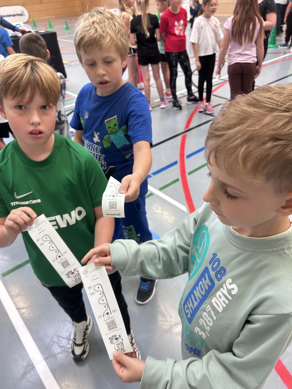 Kinder zeigen Laufkarten bei Sportstation in einer Turnhalle