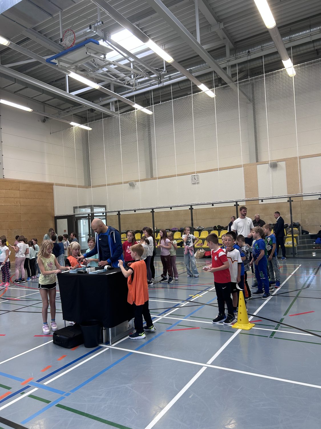 Kinder an Ausgabestand in Sporthalle mit Basketballkorb