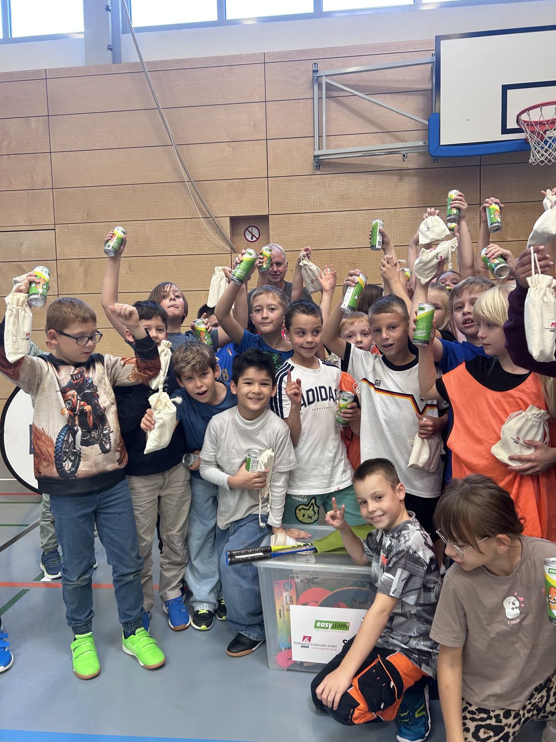 Kinder halten Getr&auml;nkedosen und Stoffbeutel in Sporthalle hoch