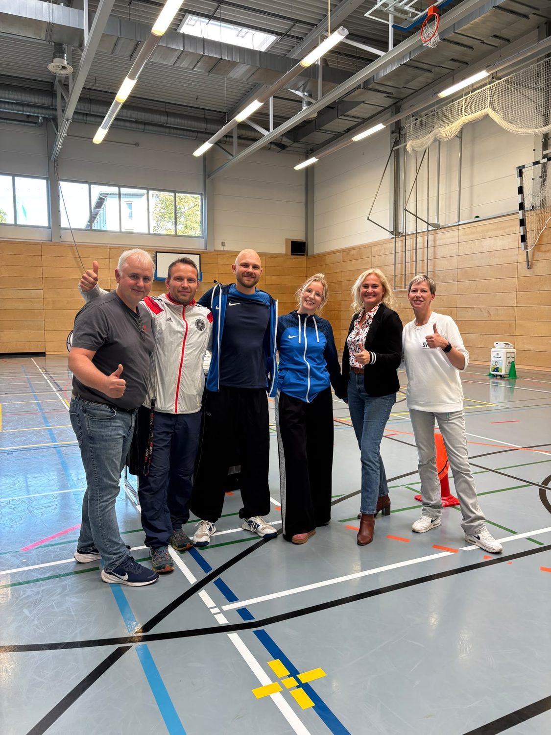 Sechs l&auml;chelnde Erwachsene in einer Sporthalle