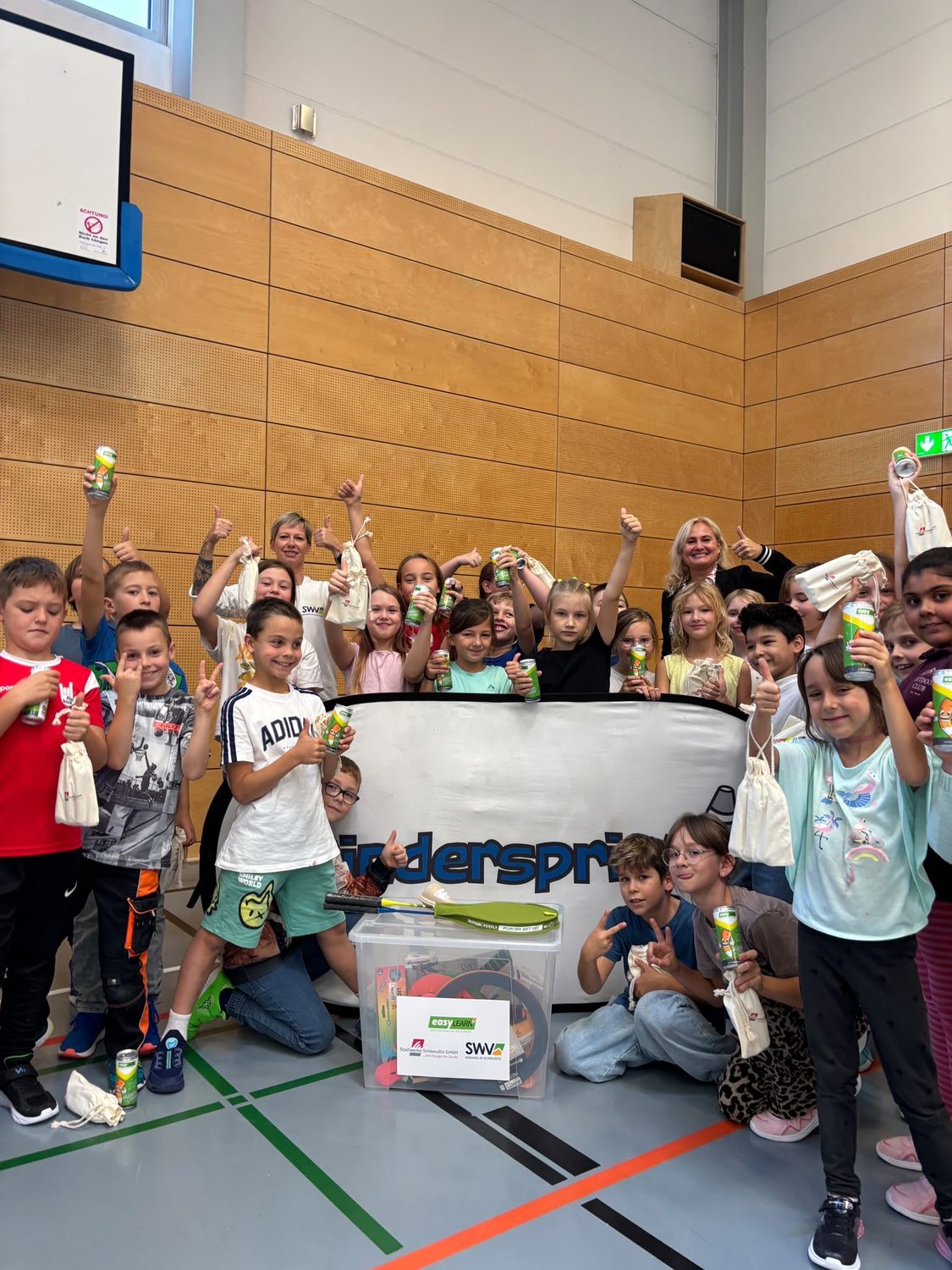 Jubelnde Kinder mit Dosen und Sportausr&uuml;stung in Turnhalle