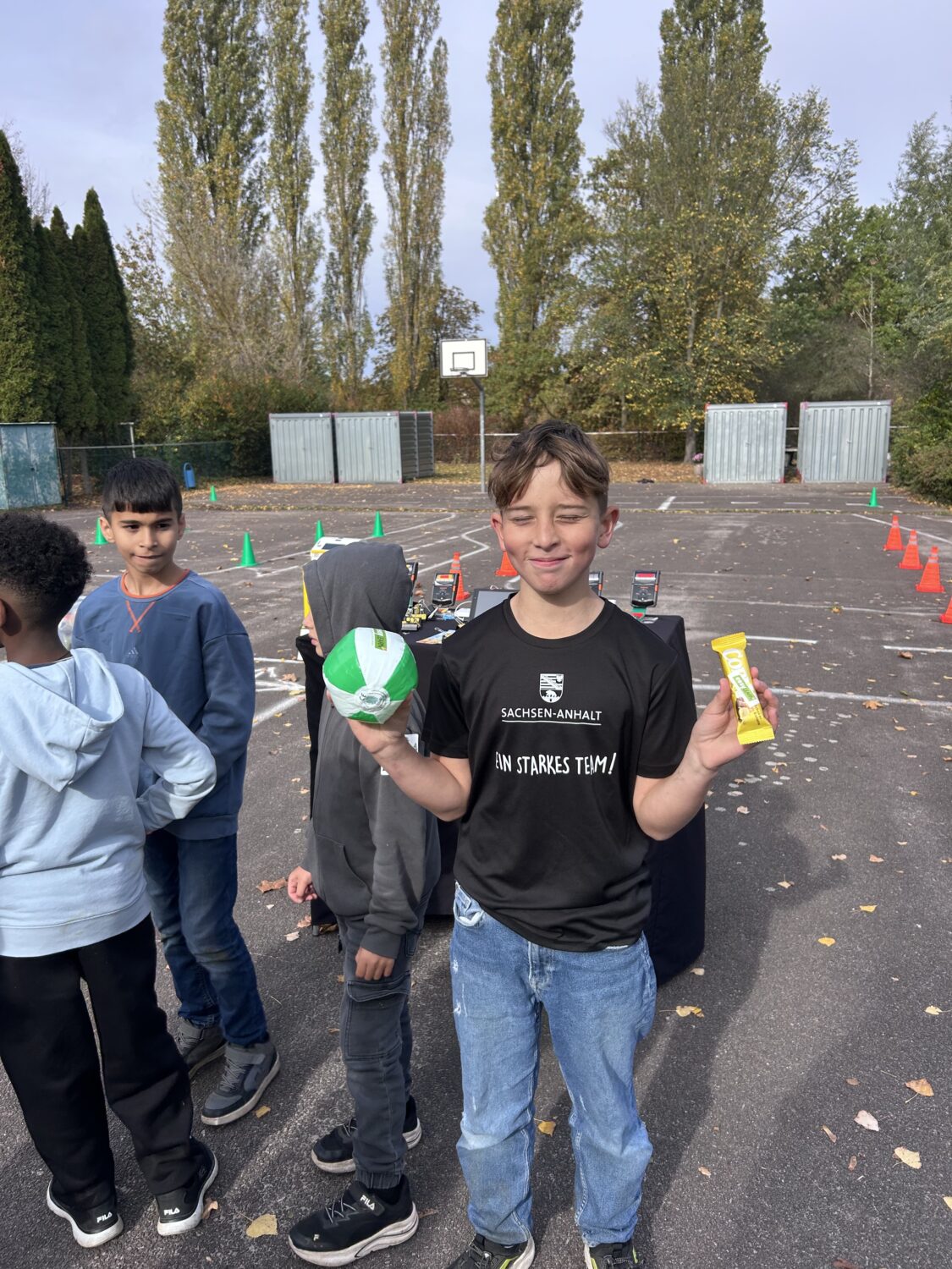 Kinder auf Schulhof mit Ball und Snack vor Parcours
