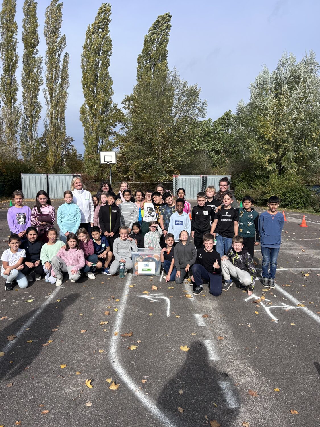 Schulklasse mit Lehrkr&auml;ften auf Basketballplatz im Herbst