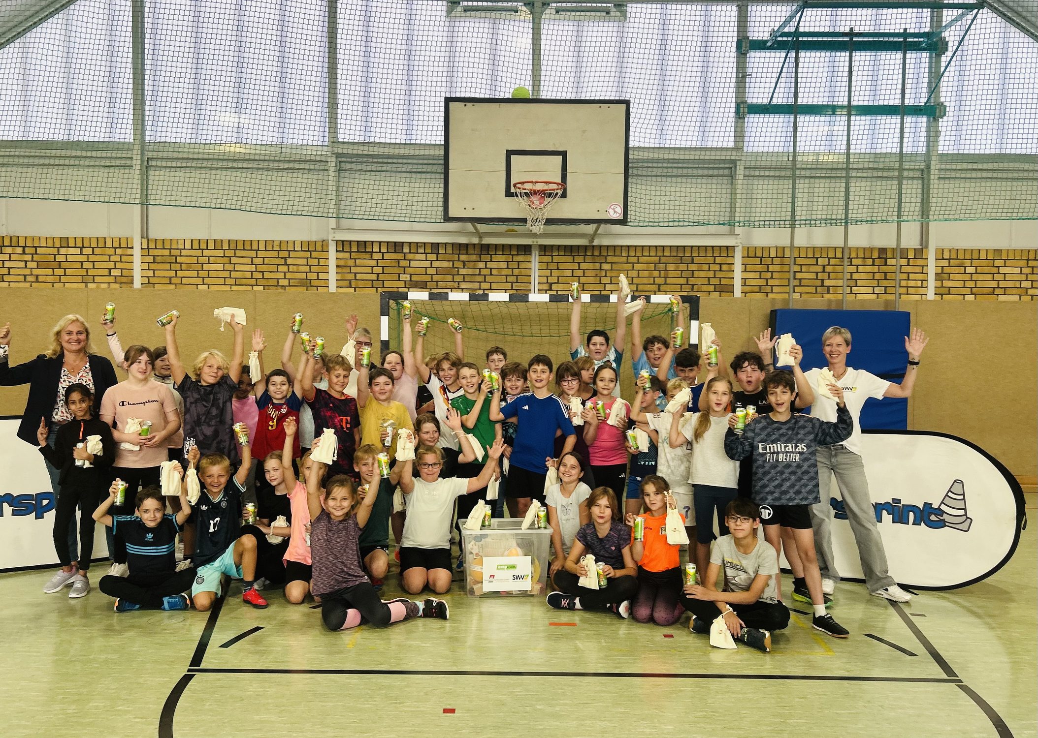 Jubelnde Kindergruppe in Sporthalle mit Getr&auml;nkedosen und Beuteln